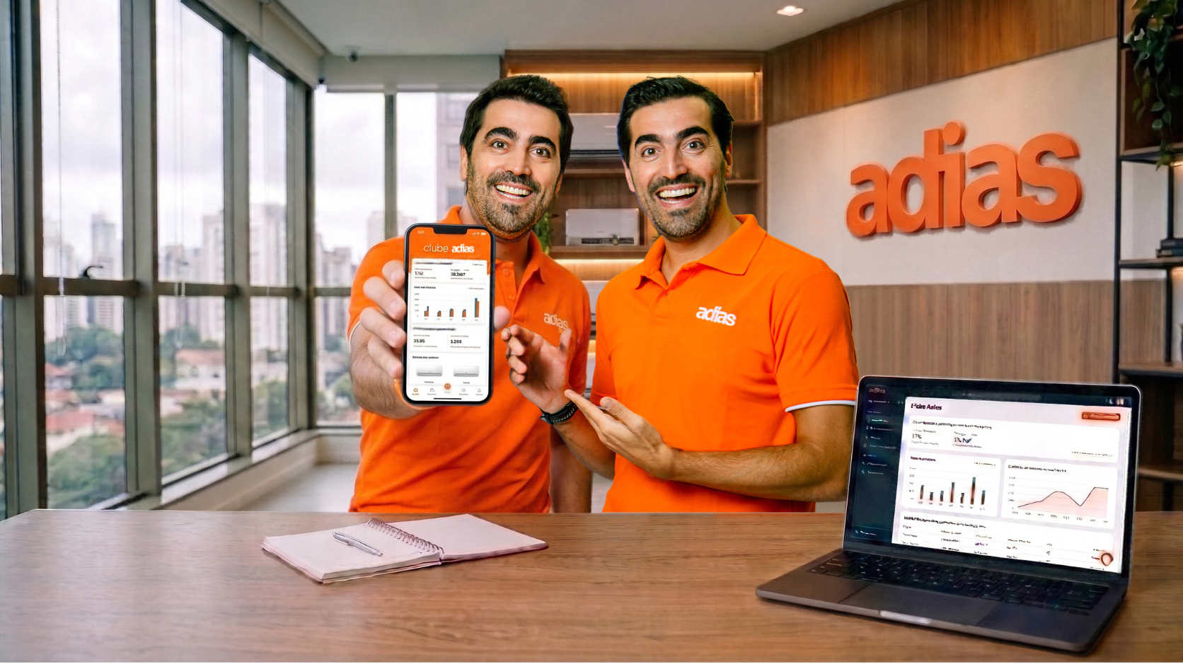 Sócios Adias no escritório apresentando o painel do Clube Adias no celular e no notebook, com o logo adias na parede